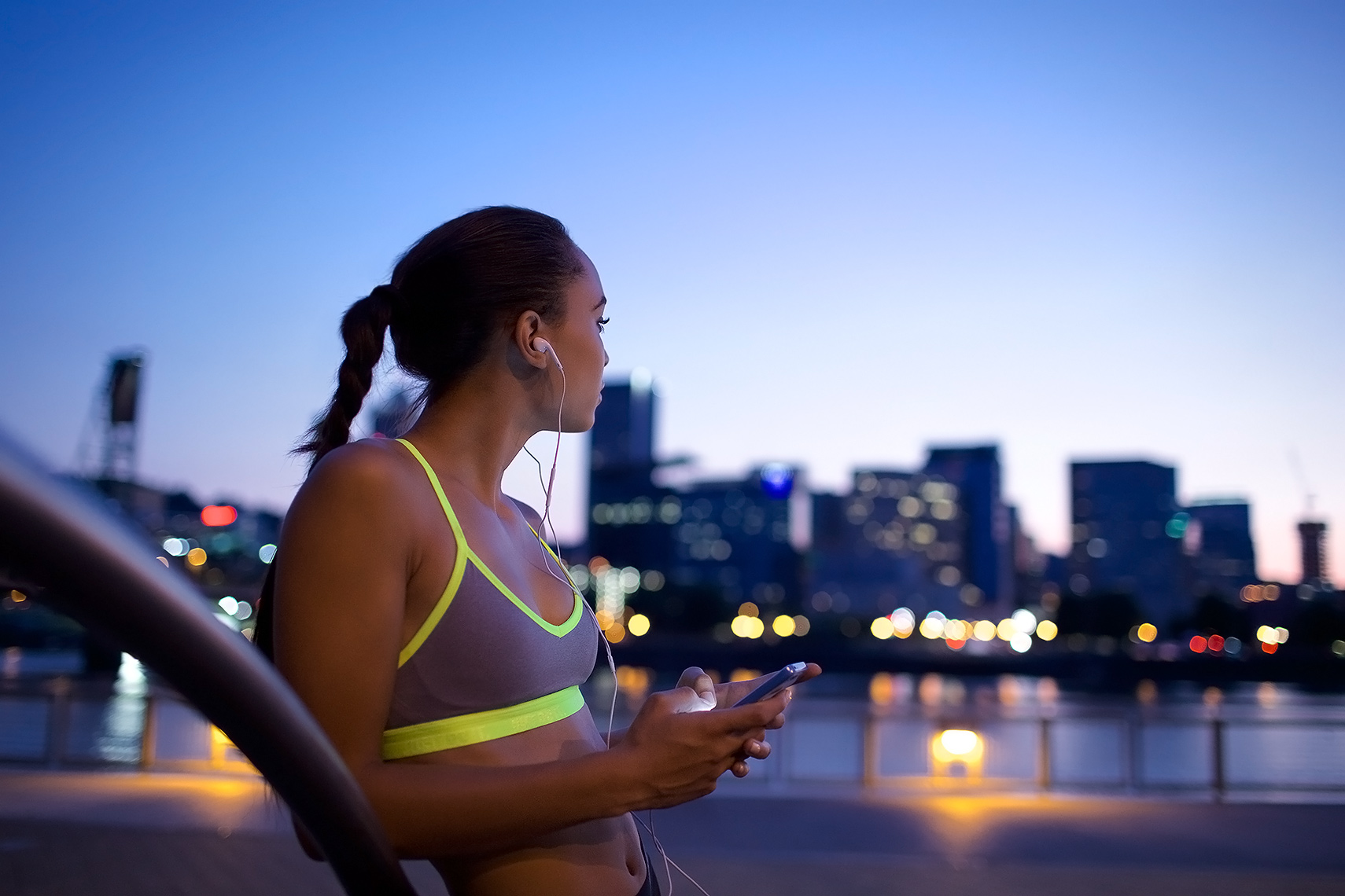 Robert-Holland_MG_9670_young woman with evening city skyline, texting after a run