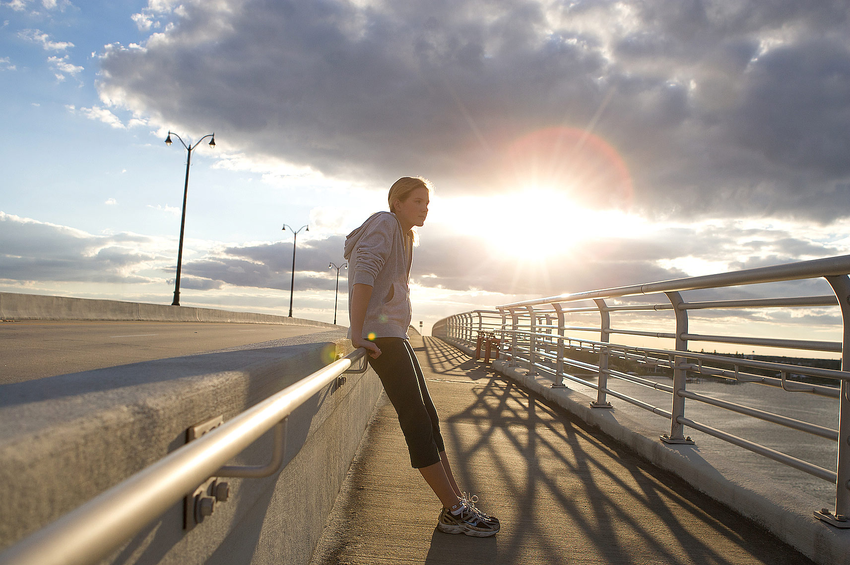 _Y0U8131_Robert_Holland__teenage runner leaning against bridge railing, resting with sunset and dramatic clouds